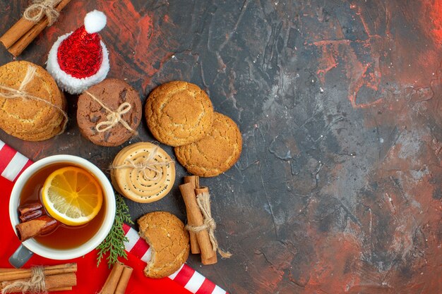 Vista dall'alto diversi biscotti tazza di tè bastoncini di cannella cappello di Babbo Natale sul tavolo rosso scuro spazio libero