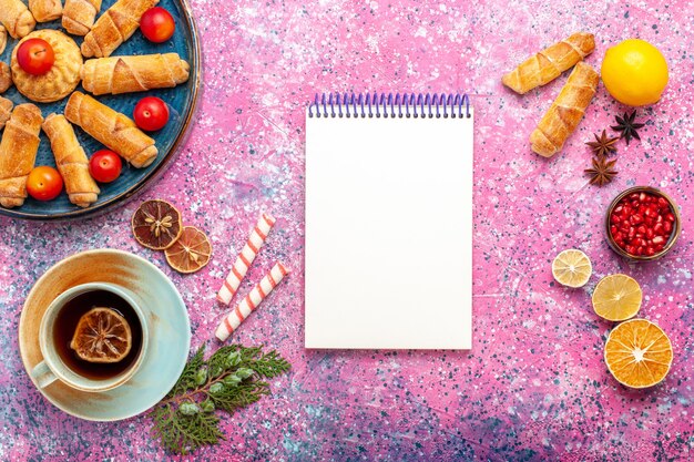 Vista dall'alto dolci deliziosi bagel all'interno del vassoio con prugne e tazza di tè sulla scrivania rosa