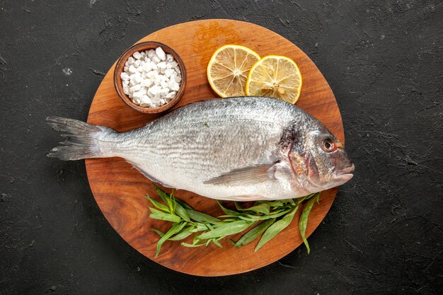 Vista dall'alto dragoncello pesce di mare crudo sale marino in una ciotola fette di limone su tavola di legno rotonda su nero