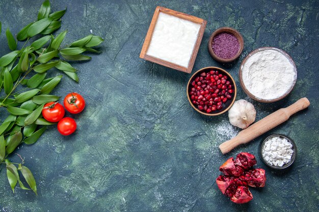 Vista dall'alto farina bianca con melograni e pomodori su sfondo blu scuro colore pasta alimentare frutta verde