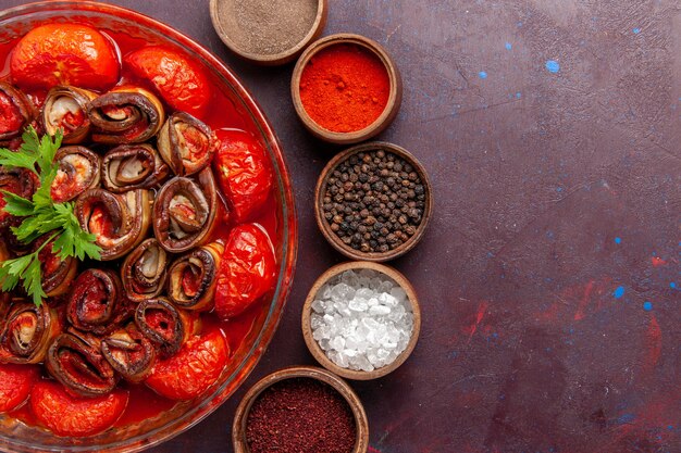 Vista dall'alto farina di verdure cotte pomodori e melanzane arrotolate e cotte con condimenti sulla scrivania scura