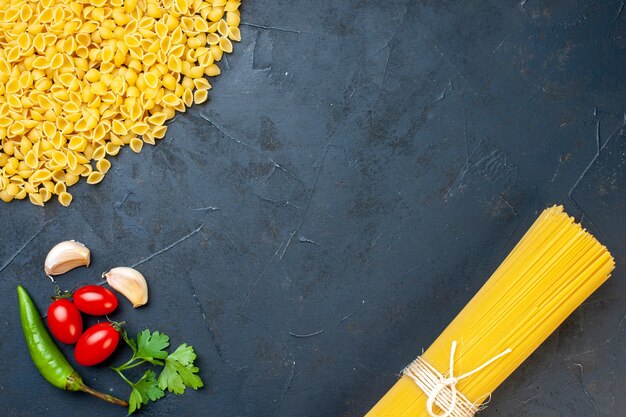 Vista dall'alto fascio di sphaggeti e conchiglie pomodorini aglio prezzemolo su sfondo scuro