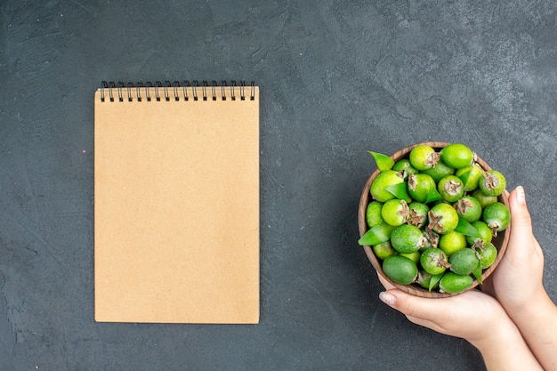 Vista dall'alto feijoas freschi nel secchio nel blocco note della mano femminile sulla superficie scura