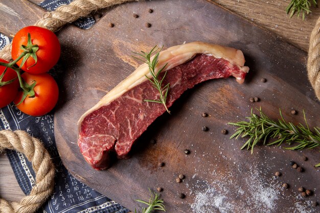 Vista dall'alto fetta di carne cruda con corde di pomodori rossi freschi e verdi sullo sfondo di legno cibo crudo foto