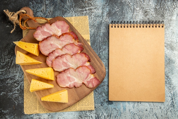 Vista dall'alto fette di carne fette di formaggio sul tagliere sul blocco note del giornale su superficie grigia gray