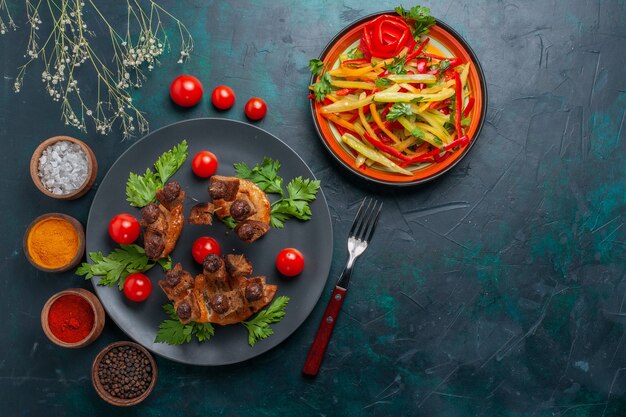 Vista dall'alto fette di carne fritta con insalata di verdure a fette e condimenti sulla salute della cena di carne di cibo pasto di verdure della scrivania blu scuro