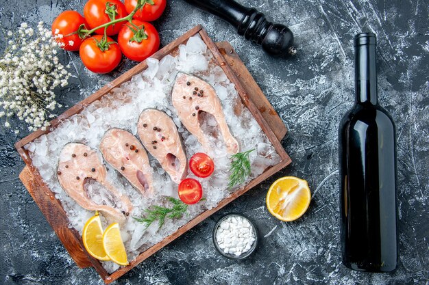 Vista dall'alto fette di pesce crudo con ghiaccio su tavola di legno pomodori macina pepe bottiglia di vino sul tavolo