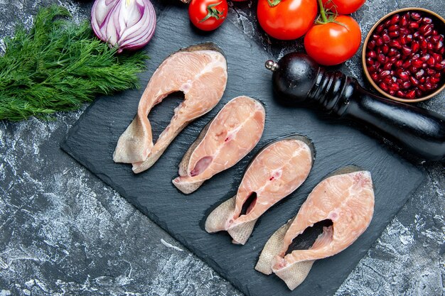 Vista dall'alto fette di pesce crudo su bordo nero aneto semi di melograno macinapepe pomodori sul tavolo