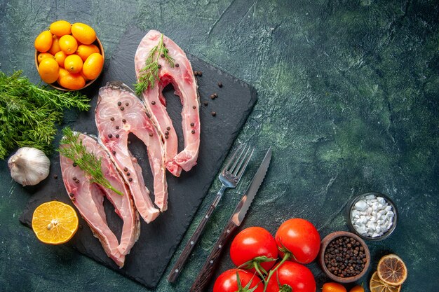 vista dall'alto fette di pesce fresco con verdi pomodori rossi e kumquat su sfondo scuro