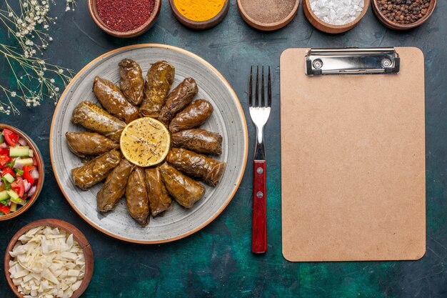 Vista dall'alto foglia dolma delizioso pasto a base di carne orientale arrotolato all'interno di foglie verdi con condimenti e verdure a fette sulla salute del piatto della cena di carne della scrivania blu