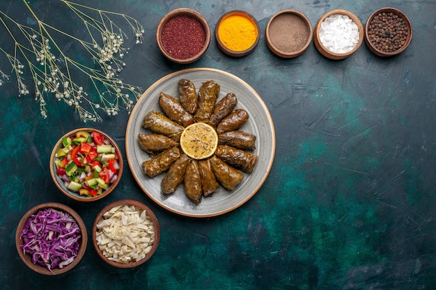 Vista dall'alto foglia dolma delizioso pasto di carne orientale arrotolato all'interno di foglie verdi con condimenti e verdure a fette sulla scrivania blu cena a base di carne piatto di salute pasto