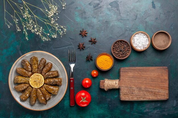 Vista dall'alto foglia dolma delizioso pasto di carne orientale arrotolato all'interno di foglie verdi con condimenti sulla scrivania blu carne cibo cena piatto vegetale salute pasto