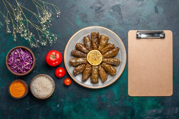 Vista dall'alto foglia dolma delizioso pasto di carne orientale arrotolato all'interno di foglie verdi con pomodori freschi su sfondo blu carne cibo cena piatto salute vegetale