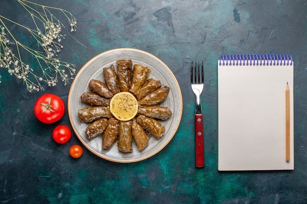 Vista dall'alto foglia dolma delizioso pasto di carne orientale arrotolato all'interno di foglie verdi con pomodori freschi sulla scrivania blu carne cibo cena piatto salute vegetale