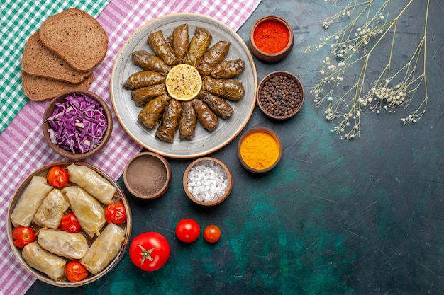 Vista dall'alto foglia dolma farina di carne orientale arrotolata all'interno di foglie verdi con condimenti e dolma di cavolo sulla scrivania blu scuro carne cena piatto pasto orientale