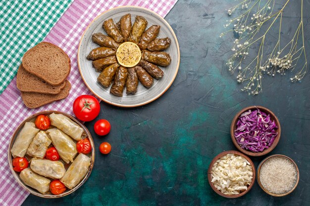 Vista dall'alto foglia dolma farina di carne orientale arrotolata all'interno di foglie verdi con pane e cavolo dolma sulla scrivania blu scuro carne cena piatto pasto orientale