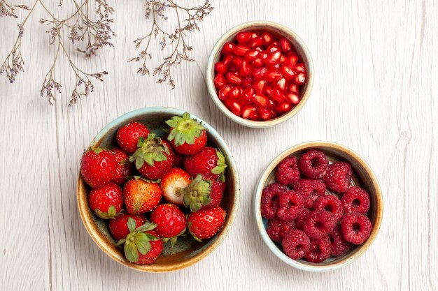 Vista dall'alto fragole fresche con lamponi e melograni su scrivania bianca bacca frutta fresca dolce maturo selvaggio