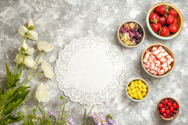 Vista dall'alto fragole rosse fresche con caramelle sui fiori di gelatina di frutta superficie bianca