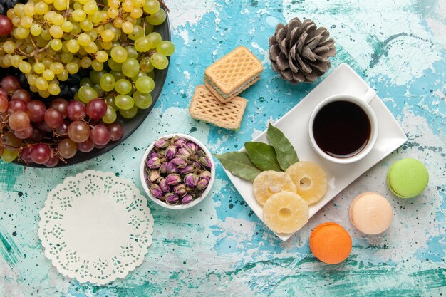 Vista dall'alto fresche uve colorate con tazza di tè macarons e cialde su sfondo blu frutti di bosco fresco mellow succo di vino