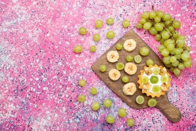 Vista dall'alto frutta fresca a fette uva e banane con torta alla crema sulla superficie viola frutta colore dolce vitamina