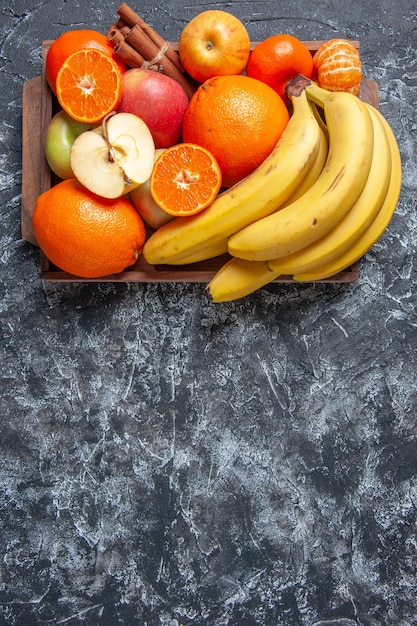 Vista dall'alto frutta fresca banane mele arance bastoncini di cannella su vassoio di legno sul tavolo con spazio libero