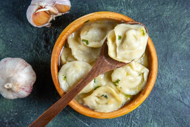 Vista dall'alto gnocchi di carne all'interno del piatto di legno con olio cipolla e aglio sulla superficie scura