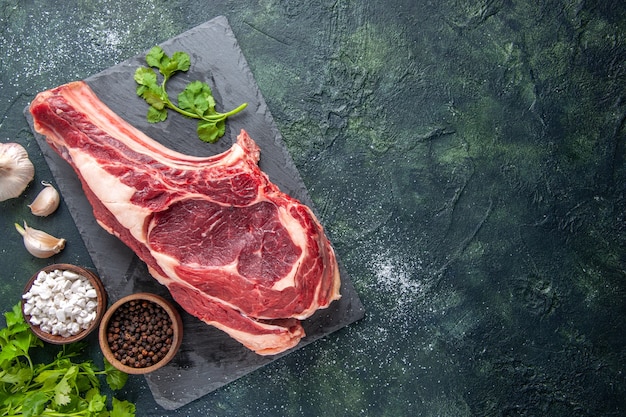 Vista dall'alto grande fetta di carne carne cruda con pepe e verdure su superficie scura