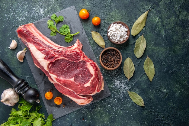 Vista dall'alto grande fetta di carne carne cruda con pepe e verdure su superficie scura