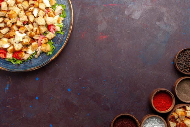 Vista dall'alto gustosa insalata caesar con diversi condimenti sulla scrivania buia