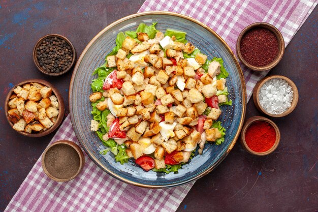 Vista dall'alto gustosa insalata caesar con piccole fette biscottate e condimenti sulla scrivania buia