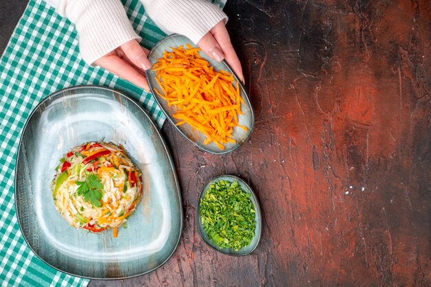 Vista dall'alto gustosa insalata di verdure all'interno del piatto con le mani femminili sul tavolo scuro