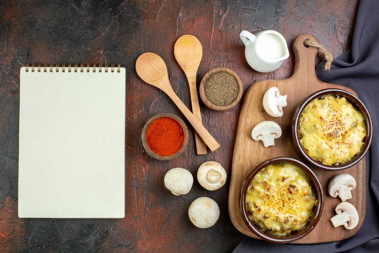 Foto gratuito vista dall'alto gustosa julienne in ciotole su tagliere cucchiai di legno spezie in piccole ciotole funghi quaderno su marrone