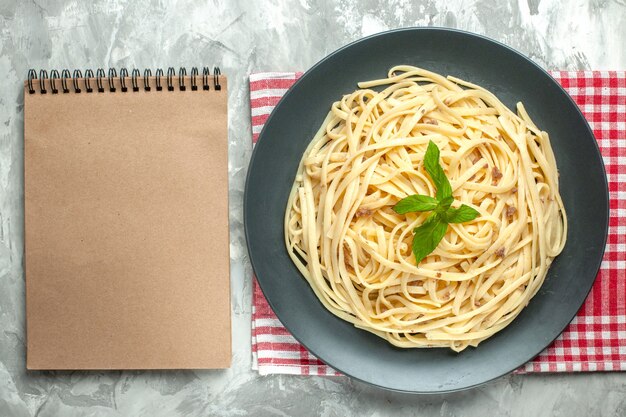 Vista dall'alto gustosa pasta italiana con blocco note su sfondo bianco