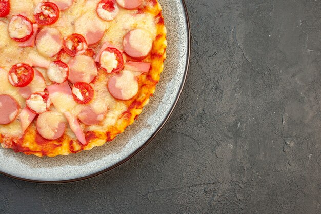 Vista dall'alto gustosa pizza al formaggio con salsicce e pomodori sul tavolo scuro