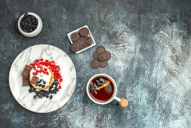 Vista dall'alto gustosa torta cremosa con biscotti al cioccolato e tazza di tè sullo sfondo chiaro-scuro