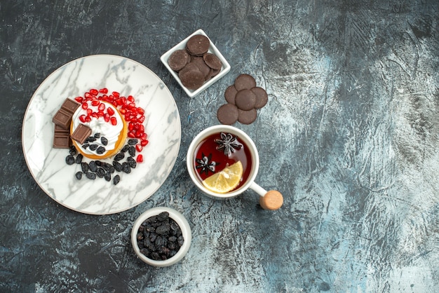 Vista dall'alto gustosa torta cremosa con biscotti al cioccolato e tazza di tè sullo sfondo chiaro-scuro