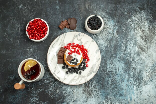 Vista dall'alto gustosa torta cremosa con biscotti al cioccolato e tazza di tè sullo sfondo chiaro-scuro