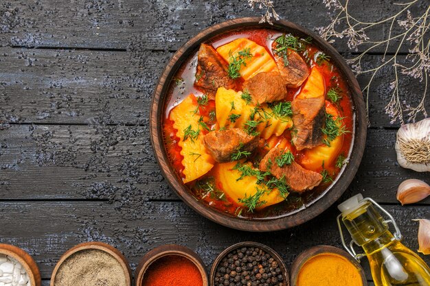 Vista dall'alto gustosa zuppa di carne con patate e condimenti sulla scrivania buia