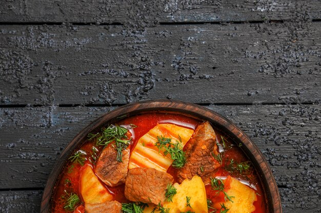 Vista dall'alto gustosa zuppa di carne con patate e verdure sulla scrivania scura