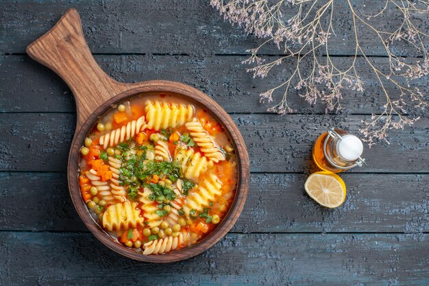 Vista dall'alto gustosa zuppa di pasta da pasta italiana a spirale con verdure sul piatto di cucina di pasta italiana color zuppa di scrivania blu scuro