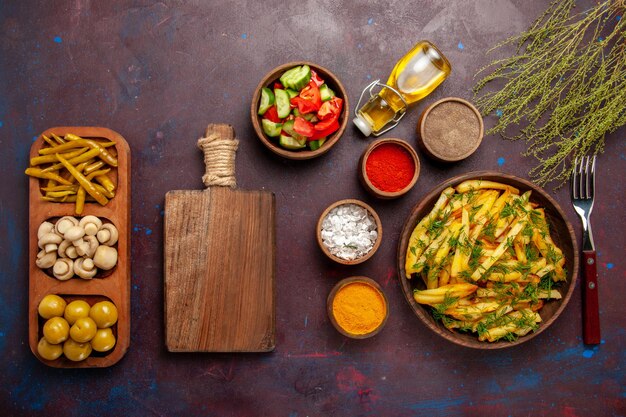 Vista dall'alto gustose patatine fritte con verdure e condimenti diversi sulla superficie scura