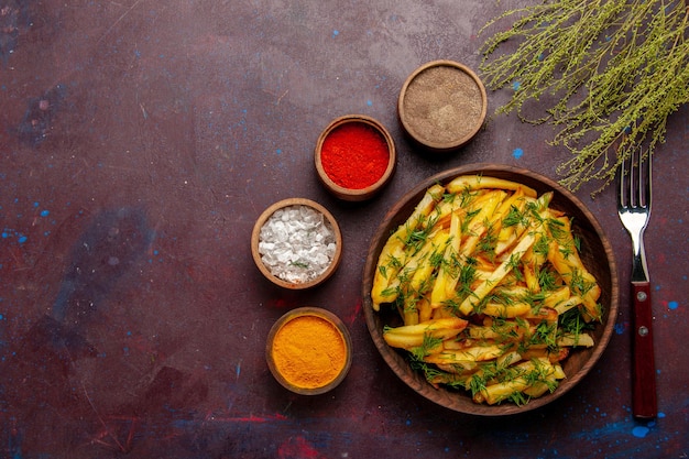 Vista dall'alto gustose patatine fritte con verdure e condimenti diversi sulla superficie scura