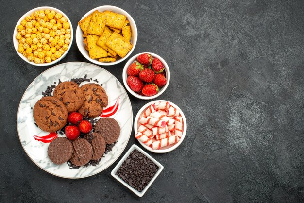 Vista dall'alto gustosi biscotti al cioccolato con diversi snack su sfondo scuro foto di biscotti dolci al tè