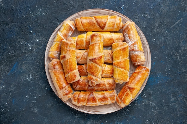 Vista dall'alto gustosi braccialetti dolci con ripieno all'interno del piatto sulla scrivania scura torta di biscotti dolci cuocere la pasticceria