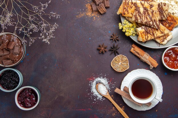 Vista dall'alto gustosi dolci con tazza di tè e marmellata su sfondo scuro pasticceria biscotto torta zucchero tè dolce