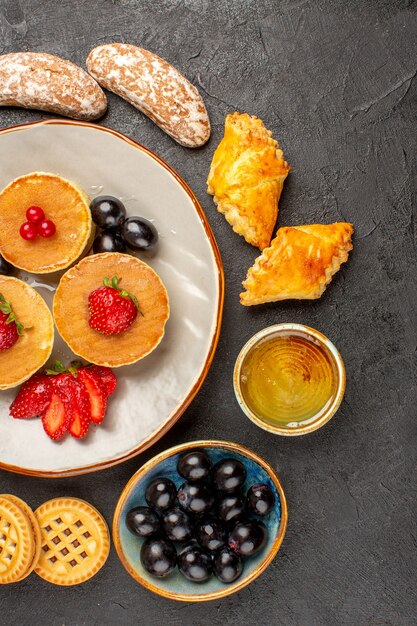 Vista dall'alto gustosi pancake con torte e frutta al buio