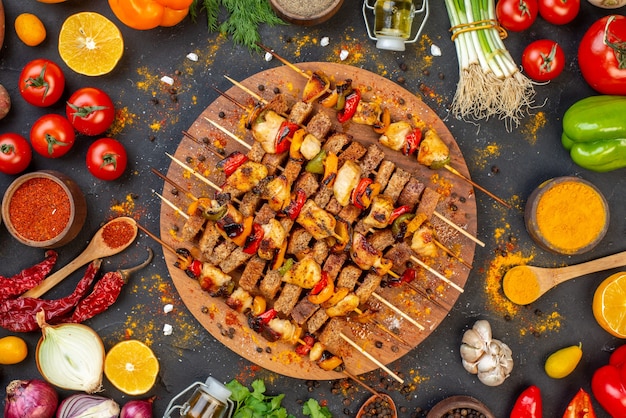 Vista dall'alto gustosi spiedini di pollo con spezie su tavola di legno e altri alimenti sul tavolo