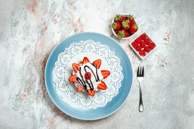 Vista dall'alto gustosissima piccola torta con panna e fragole su bianco