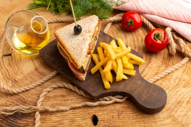 Vista dall'alto gustoso panino con prosciutto d'oliva pomodori verdure insieme a patate fritte corde olio pomodori rossi sullo sfondo di legno panino cibo spuntino colazione