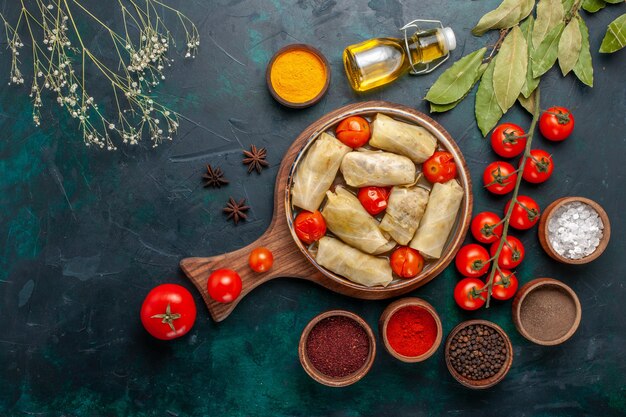 Vista dall'alto gustoso pasto di carne arrotolato all'interno di cavolo con condimenti e pomodori freschi sulla scrivania blu scuro